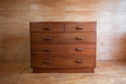 Wooden dresser with multiple drawers against a wooden wall.